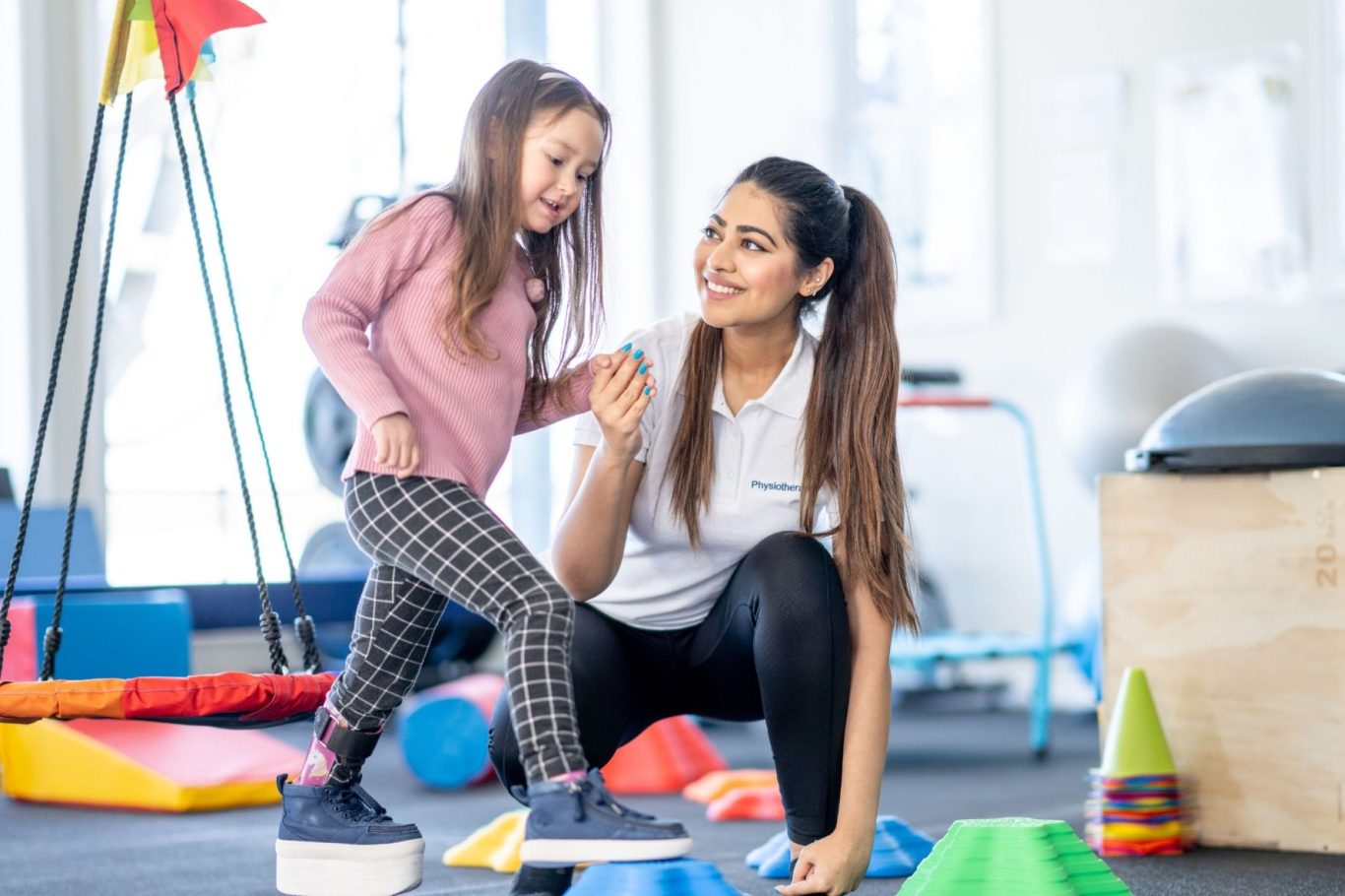 Eine Frau hilft einem Mädchen beim Spielen mit farbenfrohen Formen in einem Raum für Bewegung.
