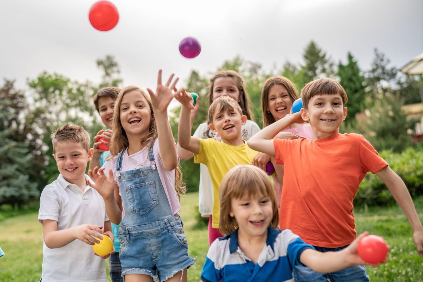 Eine Gruppe von Kindern spielt fröhlich mit bunten Bällen im Freien.