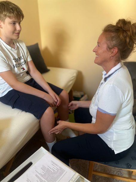 Ein Kind sitzt auf einer Couch, während eine Frau ihm gegenüber sitzt und lächelt.