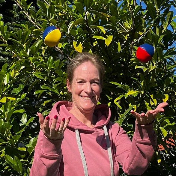 Stephanie Voigt - Das bin ich Stephanie Voigt in rosa Hoodie jongliert mit bunten Bällen vor einer grünen Hecke.