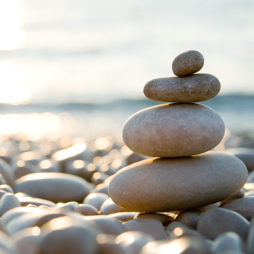 Drei sorgfältig gestapelte Steine am Ufer eines Gewässers.